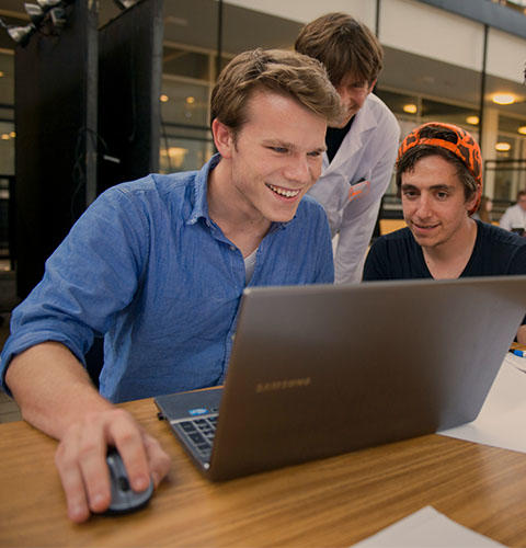 Three students smile while one is working on a laptop